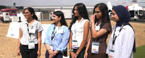 all-female team wearing business clothing. background are a bunch of fire trucks and airplanes.