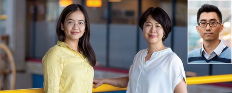 Two women stand together near a yellow railing in a modern indoor space. A smaller image of a man is inset in the corner.