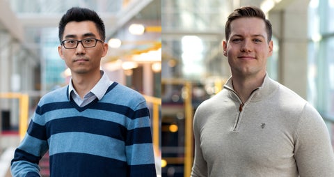 Two men stand side by side in a brightly lit indoor space. The man on the left wears a blue and gray striped sweater, while the man on the right is dressed in a light gray zip-up sweater.