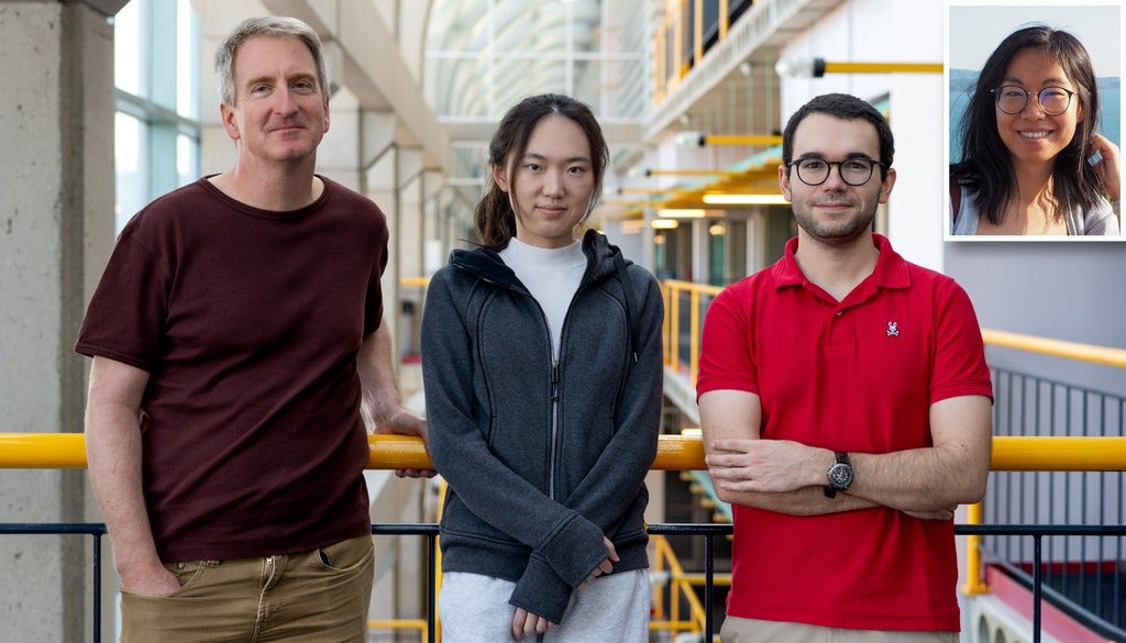 Three individuals stand together in an indoor space with a modern design, featuring large windows and yellow railings. A smaller inset image of a person is visible in the corner.