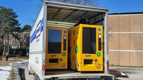 Photo of a truck. The back is open showing the truck is hosting 2 M&M themed vending machines