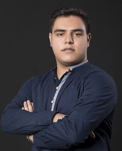 A South Asian male wearing a navy blue dress shirt, crossing his arms in front of his chest. The background is black