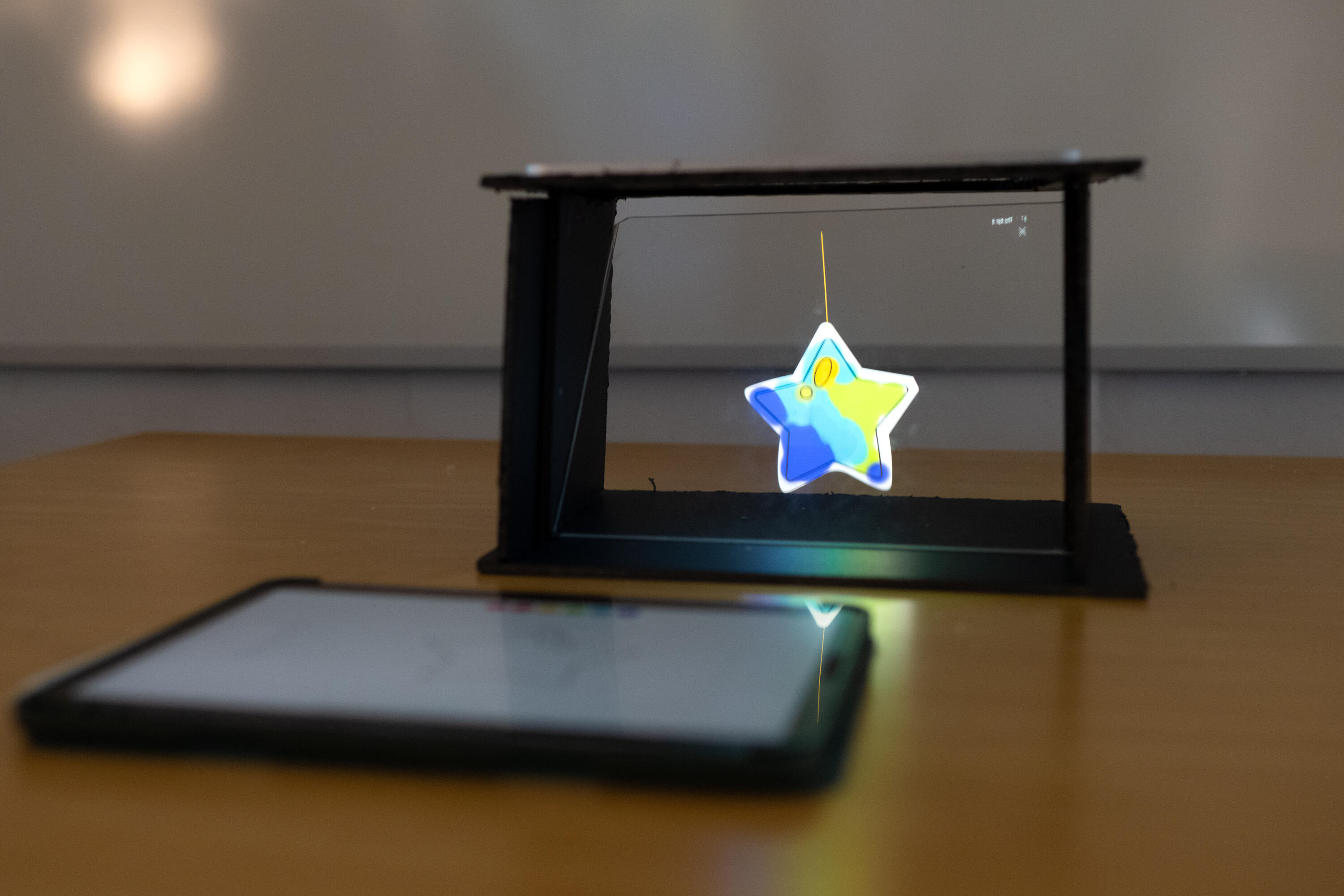 there's an iPad lying flat. There's a plexi screen that has a hologram of a blue-green-yellow star propped by a string
