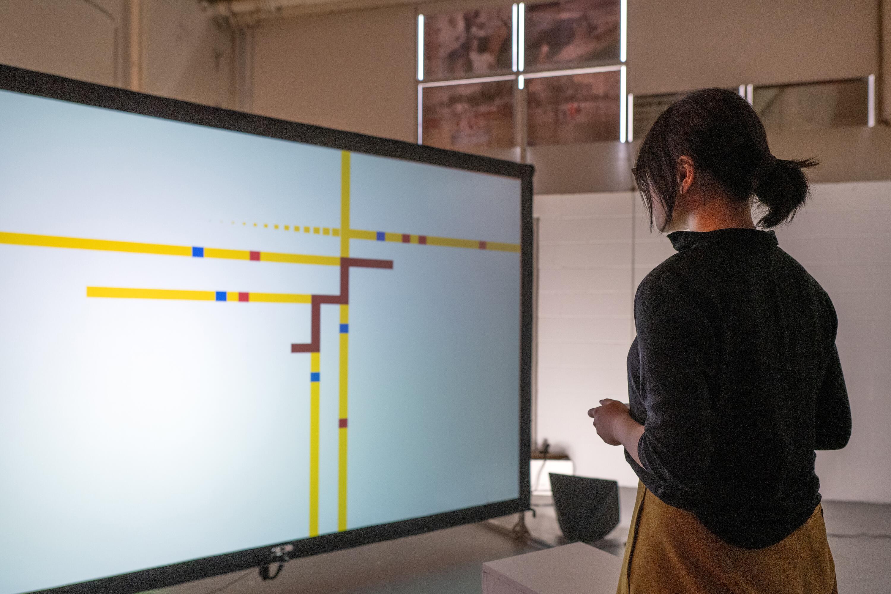 standing in front of a screen holding a controller. back is facing the camera
