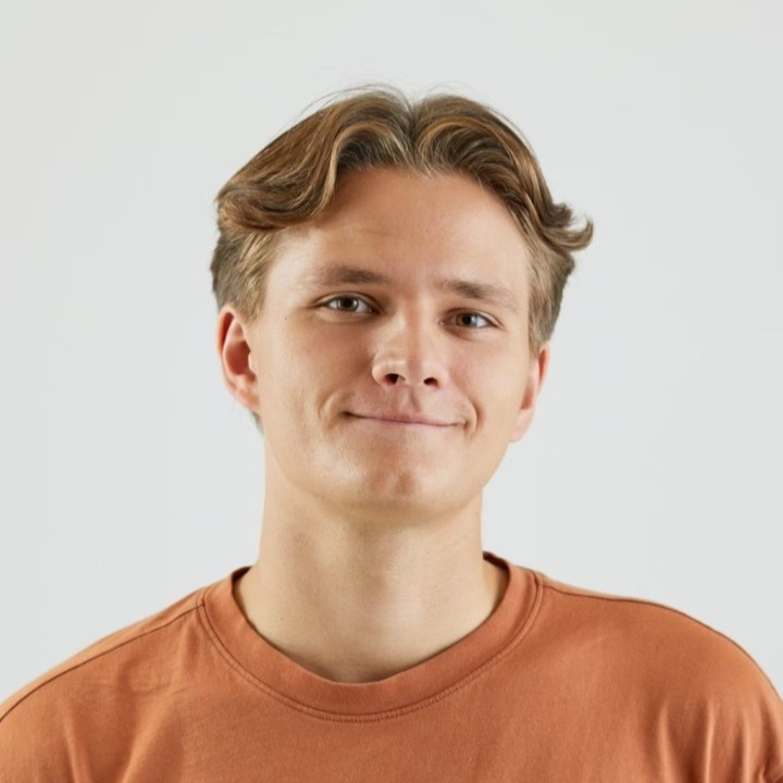 a brunette man wearing an orange shirt posing aganist a white background