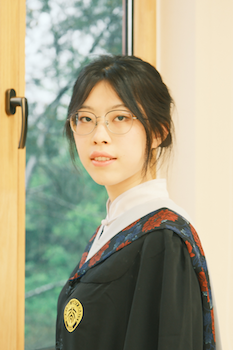 high-contrast image of an asian woman wearing a graduation robe and glasses