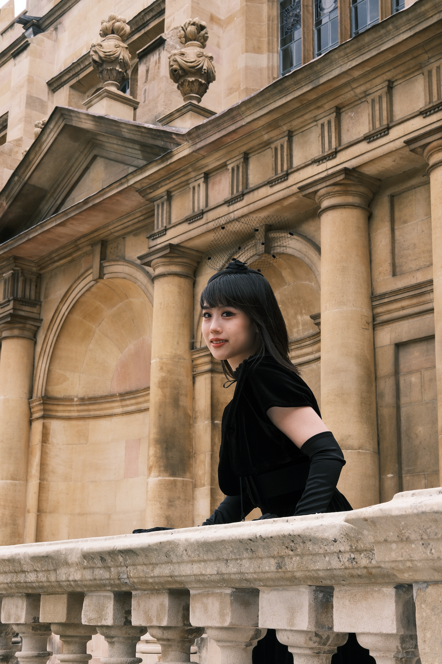 An Asian woman dressed in black aganist a castle-like backdrop